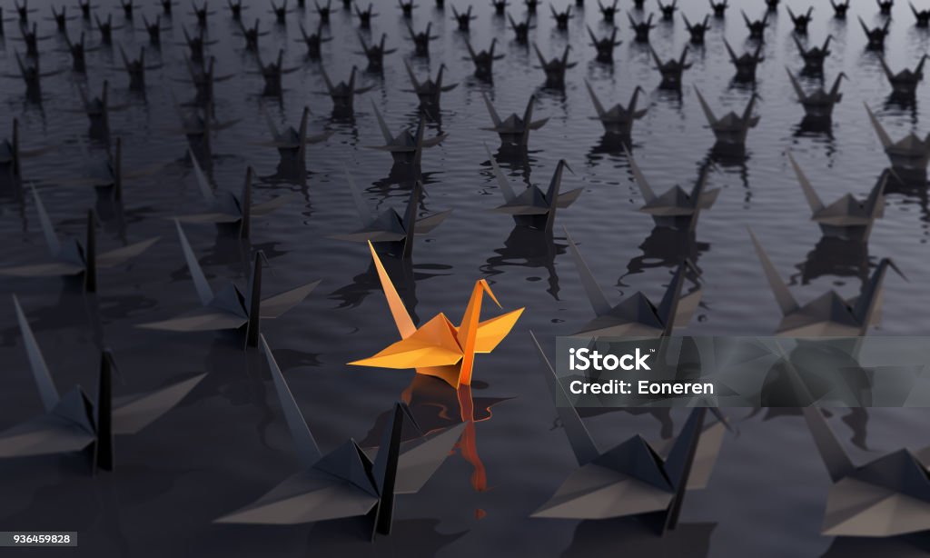 Standing Out From The Crowd With Paper Cranes Standing out from the crowd concept with an orange colored paper crane between the black ones on the water. ( 3d render ) Concepts Stock Photo