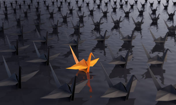 Standing Out From The Crowd With Paper Cranes Standing out from the crowd concept with an orange colored paper crane between the black ones on the water. ( 3d render ) origami stock pictures, royalty-free photos & images