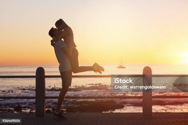Young Woman Jumps Into Boyfriends Arms And Gives Him A Kiss At Sunset Stock Photo - Download Image Now