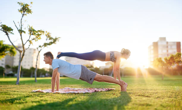 vestibilità acrobatica e coppia di yoga sana che si allea nel parco insieme - sunset yoga young men caucasian foto e immagini stock