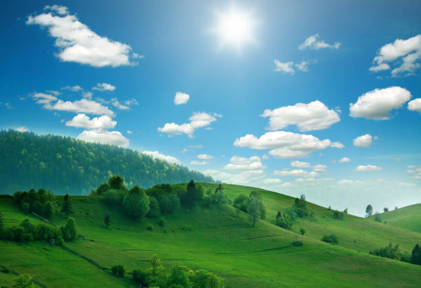 istock Mountain hills and green fields in sunlight on sky clouds 936472646