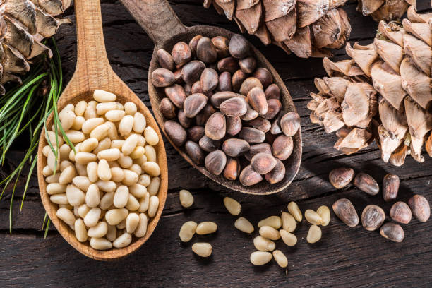 istock Pine nuts in the spoon and pine nut cone on the wooden table. 936473916
