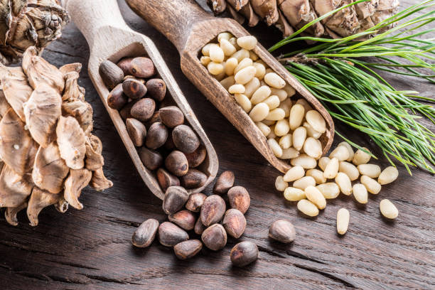istock Pine nuts in the spoon and pine nut cone on the wooden table. 936474274