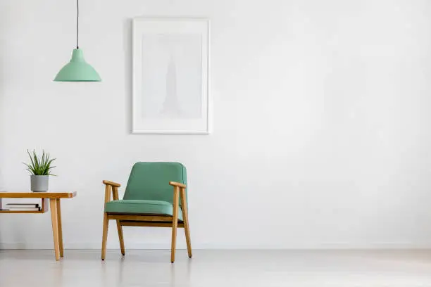 Retro concept mint pastel armchair, wooden table and framed poster in a bright minimalist interior with copy space