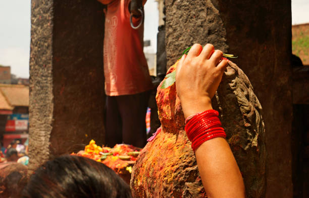Close up of an ancient sandstone shrine and weathered lion statue with colorful religious offerings. The hand of a nepalese woman is placing an offering directly on top of the lions head. She is wearing the traditional red glass bracelets around her wrist to symbolize the bonding with her husband. Blossoms, rice, green leafs, red and yellow pigment powder and much more is used by the nepalese people celebrating their religious hinduistic ceremonies and cultural beliefs. Statue and altar are part of the Dattatraya temple on Tacapal square in old town Bhaktapur. Hinduism. Asian culture, spirituality and religion. XXXL Sony Alpha 7R.