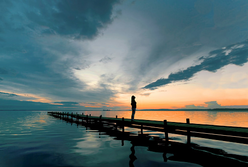 Silueta de mujer de pie en el muelle junto al lago al anochecer viendo cloudscape majestuoso photo
