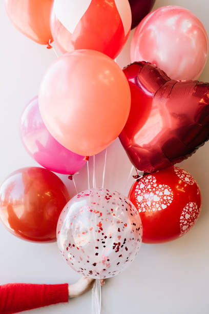 istock Womans hand (in a red sweater) holding a bundle of colourful balloons (pink, red,crimson) on the grey wall background 936573504