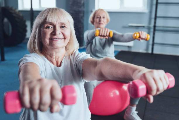 istock Charming elderly woman smiling for camera while lifting dumbbells 936575800