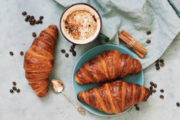 Photo of Fresh croissants, together with espresso coffee on a blue background. The view from the top.