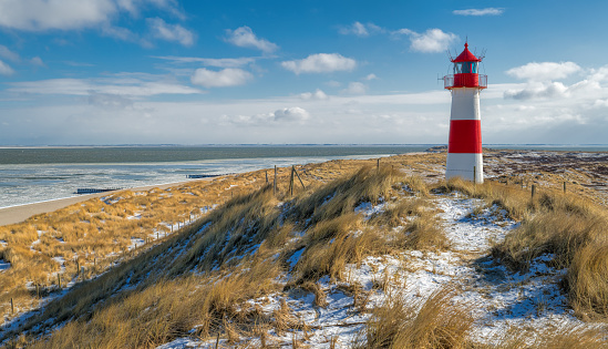 Red and white Lighthouse on sand dune with marram grass in snow.
Location: Ellenbogel in the north of Island Sylt, Germany