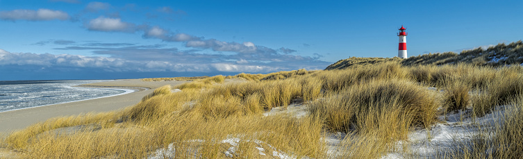 Red and white Lighthouse on sand dune with marram grass in snow.\nLocation: Ellenbogel in the north of Island Sylt, Germany