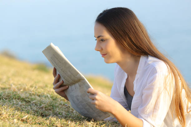 istock Girl reading a newspaper on the grass 936583982