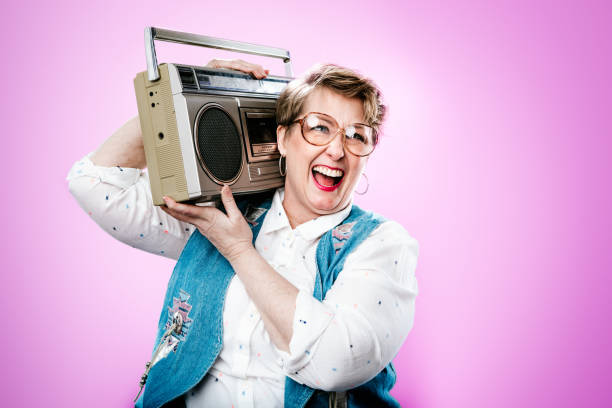 Nineties Styled Woman Portrait With Boombox Stereo A portrait of a  woman wearing clothing and accessories from the 1990's, a bright pink colored background behind her.  She holds a personal stereo system on her shoulder. stereo photos stock pictures, royalty-free photos & images