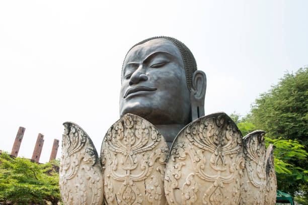 In the historic UNESCO city of Ayuthaya, Thailand, a large black Buddha head is surrounded with the petals of a lotus flower sculture and is placed outside the temple grounds.