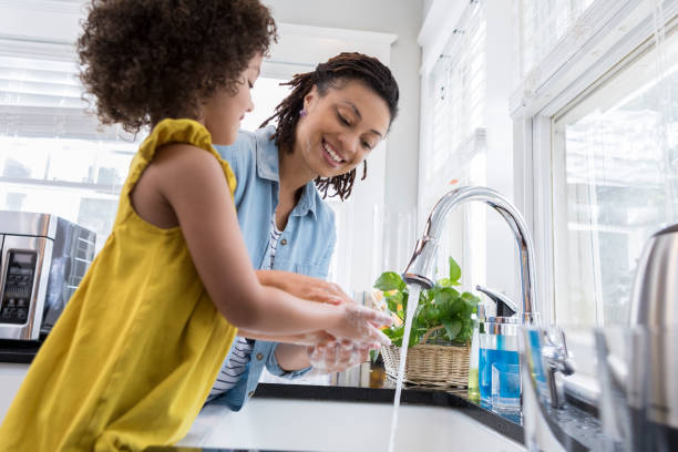 Mom helping young daughter wash hands Beautiful mom and her adorable daughter wash their hands after baking in the kitchen. kitchen sink photos stock pictures, royalty-free photos & images