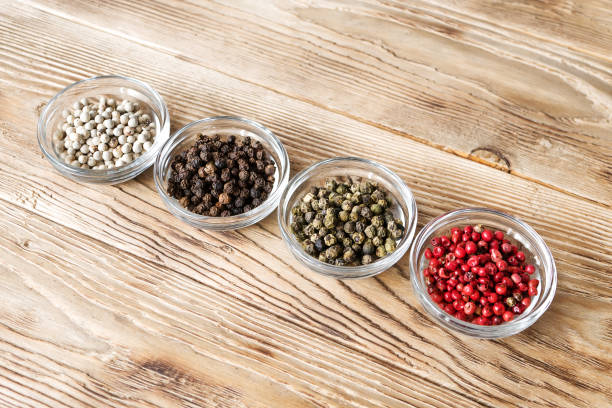 différents types de grains de poivre. quatre variantes de poivre vert en plaques de verre sur fond rustique. poivre noir, blanc, vert et rose. baies séchées utilisé comme épice et assaisonnement. photo de nourriture. - directly above macro pepper black peppercorn photos et images de collection