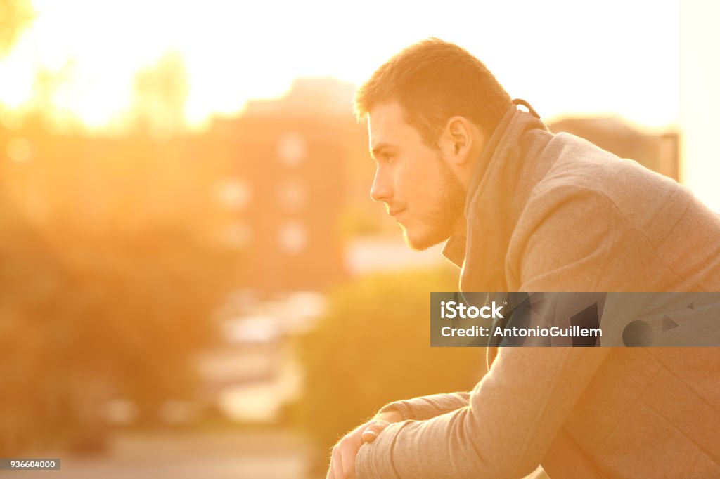 Serious man looking away at sunset in winter Side view portrait of a serious man looking away in a balcony at sunset in winter Men Stock Photo