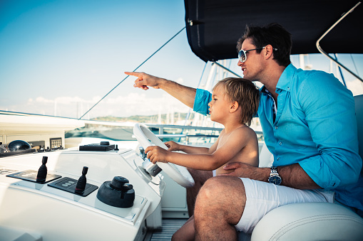 Father teaches his young son how to steer a yacht.