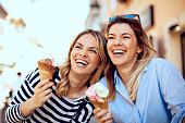 Two young women laughing and holding ice cream in hand