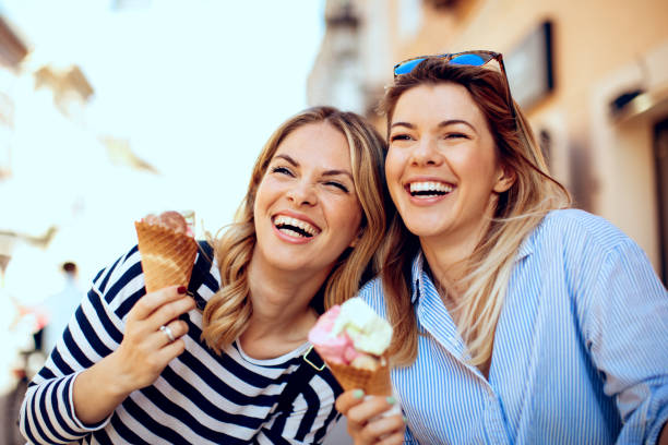 Two young women laughing and holding ice cream in hand stock photo