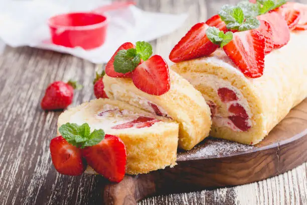 Homemade strawberry shortcake cake roll with cream cheese whipped cream, perfect summer season dessert served on rustic wooden board