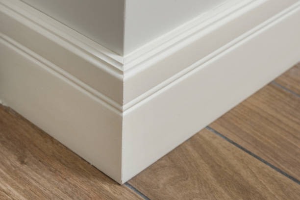 Molding in the interior, baseboard corner. Light matte wall with tiles immitating hardwood flooring Molding in the interior, baseboard corner. Light matte wall with tiles immitating hardwood flooring. architectural cornice stock pictures, royalty-free photos & images