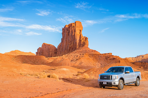 Pickup truck drives past scenic cliffs at the Monument Valley loop drive, Utah on a sunny day.
