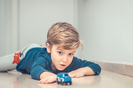 Playful kid having fun with car toy on the floor.