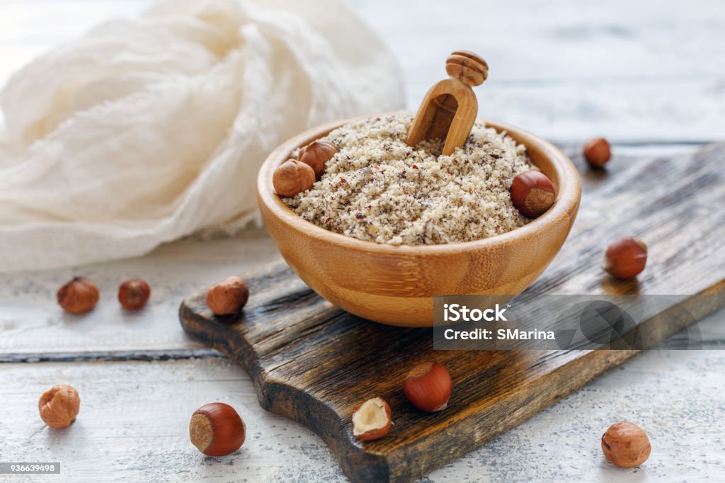 Hazelnut flour in wooden bowl and whole hazelnut. Bowl with hazelnut flour on an old white wooden table. Backgrounds Stock Photo