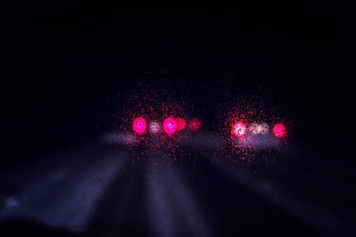 Dark stormy winter night car driver point of view perspective looking through icy, blurred windshield toward a group of traffic vehicles speeding up ahead.