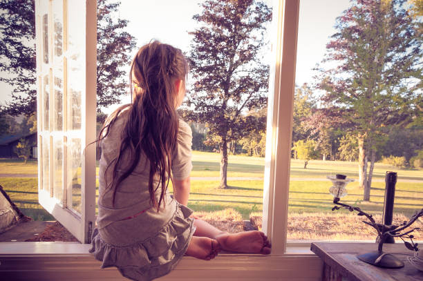 bambina che guarda fuori dalla finestra della sua camera da letto da sola - outdoors looking at camera little girls child foto e immagini stock