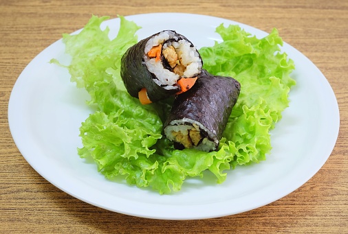 Japanese Cuisine, Traditional Vegetarian Japanese Rice Maki Sushi Roll Stuff with Tofu and Carrot Wrapped in Nori Seaweed Served on Green Oak.