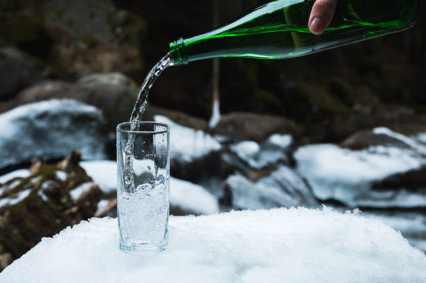 se vierte agua mineral mineral de una botella de vidrio verde en un vaso de vidrio transparente - water flowing water pouring ice fotografías e imágenes de stock