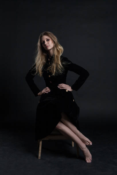 istock Full length model in black dress posing sitting on dark background 936665360