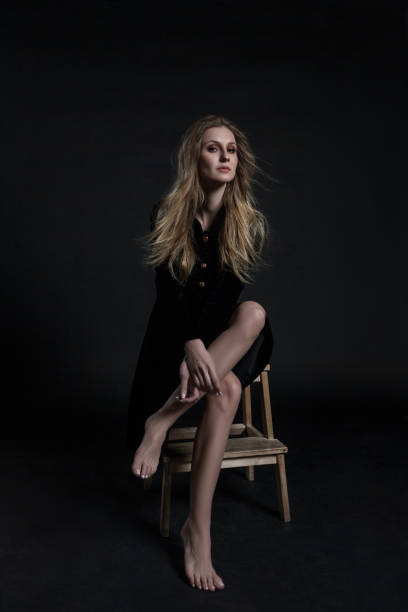 istock Full length model in black dress posing sitting on dark background 936669972