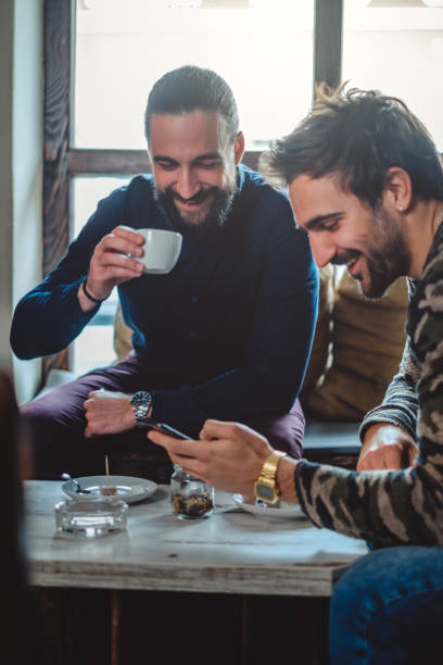 Smiling friends drinking coffee and looking at the mobile phone stock photo