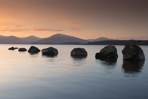Stones leading into the calm and peaceful waters of Loch Lomond at sunset.