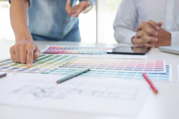 istock Two interior design or graphic designer at work on project of architecture drawing with work tools and color swatches, colour chart, color samples for selection, renovation and technology concept 936694214