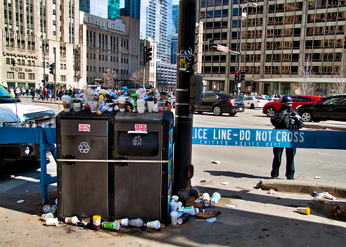 Garbage overflows out of trash receptacles on Michigan Avenue during St. Patrick's Day festivities.  Police barrier in view.