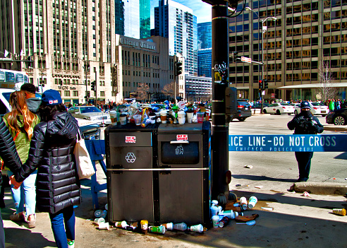 Garbage overflows out of trash receptacles on Michigan Avenue during St. Patrick's Day festivities.  Police barrier in view.