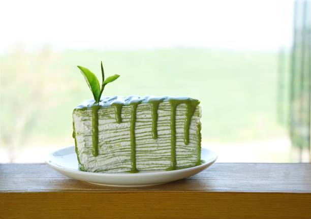 Piece of green tea crape cake on white plate and decorated with fresh tea leaf stock photo