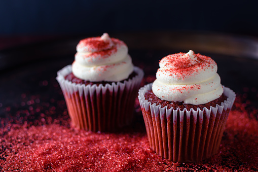 Closeup gourmet delicious red velvet cakes on a pile of red candy sprinkles; useful for bakery, eatery, grocery advertisements;