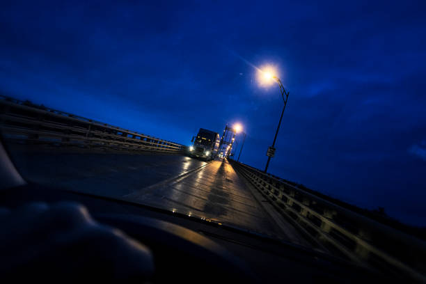 Night car driver point of view looking through windshield at approaching semi tractor trailer trucks on the Interstate Route 81 Thousand Islands Bridge; a USA Canada border crossing over the Saint Lawrence River.