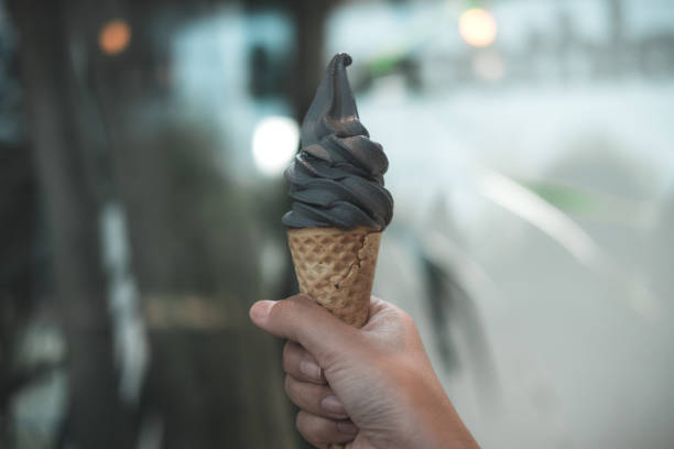рука, держащая конус мороженого древесного угля с размытием фона - melting ice cream cone chocolate frozen стоковые фото и изображения