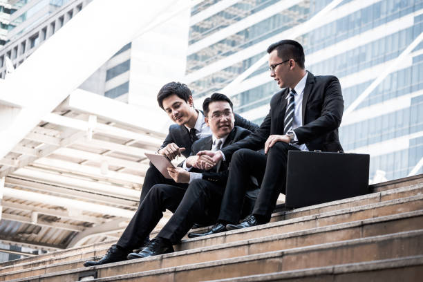 istock Cheerful group of young business men shaking hands together after new project success while sitting on stairs in front of the office building. 936746122