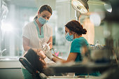 Dentist and her assistant performing dental drilling on young woman.