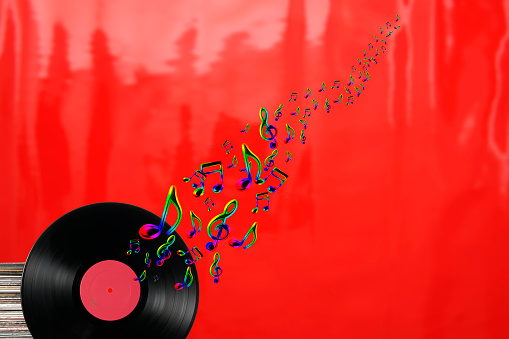 Vinyl record with lots of colorful flying musical notes against red background, with copy space.