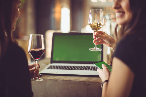 Colleagues toasting with wine in restaurant, green screen laptop in background