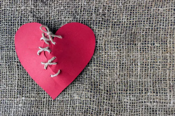 A broken red heart. Sewn thread. The concept of divorce, separation.