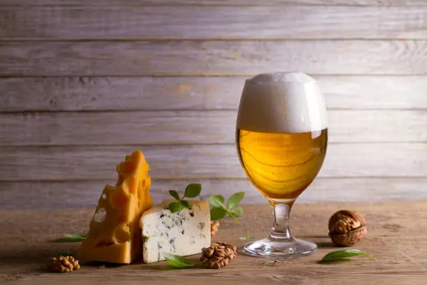 Beer and cheese. Glass of beer with cheese, walnuts and basil on wooden background. Ale and food concept